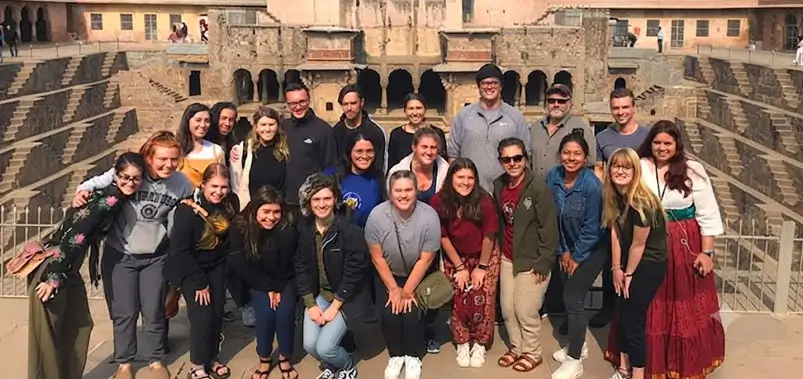 Large group of diverse tourists posing together on the stone step of a historic stepwell site