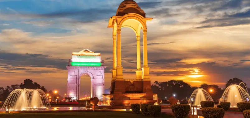 Illuminated India Gate war memorial and canopy with glowing fountains at sunset