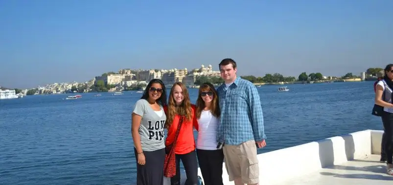 Group of friends enjoying a scenic boat ride on Lake Pichola with Udaipur City Palace in the background.