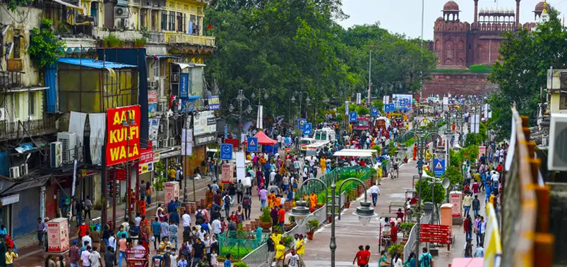 Busy street market scene in Chandni Chowk Delhi with crowded pedestrians shops and the Red Fort visible in the background