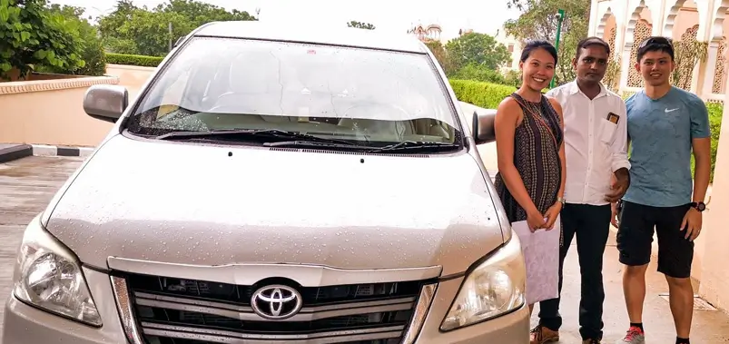 Friendly tourist couple posing with their personal driver in front of a white Toyota tour car in India.
