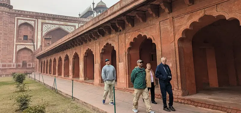Group of tourists walking along the corridor of a historic red sandstone fort with ornate arched architecture