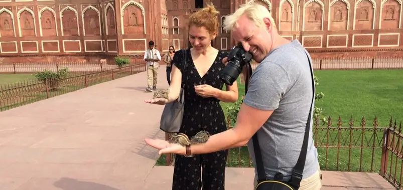 Tourists feeding friendly palm squirrels on a walkway at a historic Indian monument